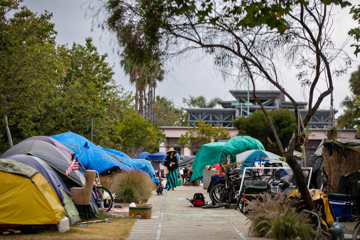 A woman walks down the long row of tents at a homeless encampment.