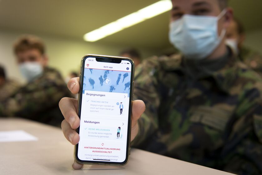 A soldier of the Swiss army wearing a protective face mask holds a smartphone with an app using Decentralized Privacy-Preserving Proximity Tracing (DP-3T) during a test with 100 soldiers in the military compound of Chamblon near Yverdon-les-Bains, Switzerland, Thursday, April 30, 2020. The race by governments to develop mobile tracing apps in order to contain infections after lockdowns ease is focusing attention on privacy. The debate is especially urgent in Europe, where academics and civil liberties activists are pushing for solutions that protect personal data. (Laurent Gillieron/Keystone via AP)
