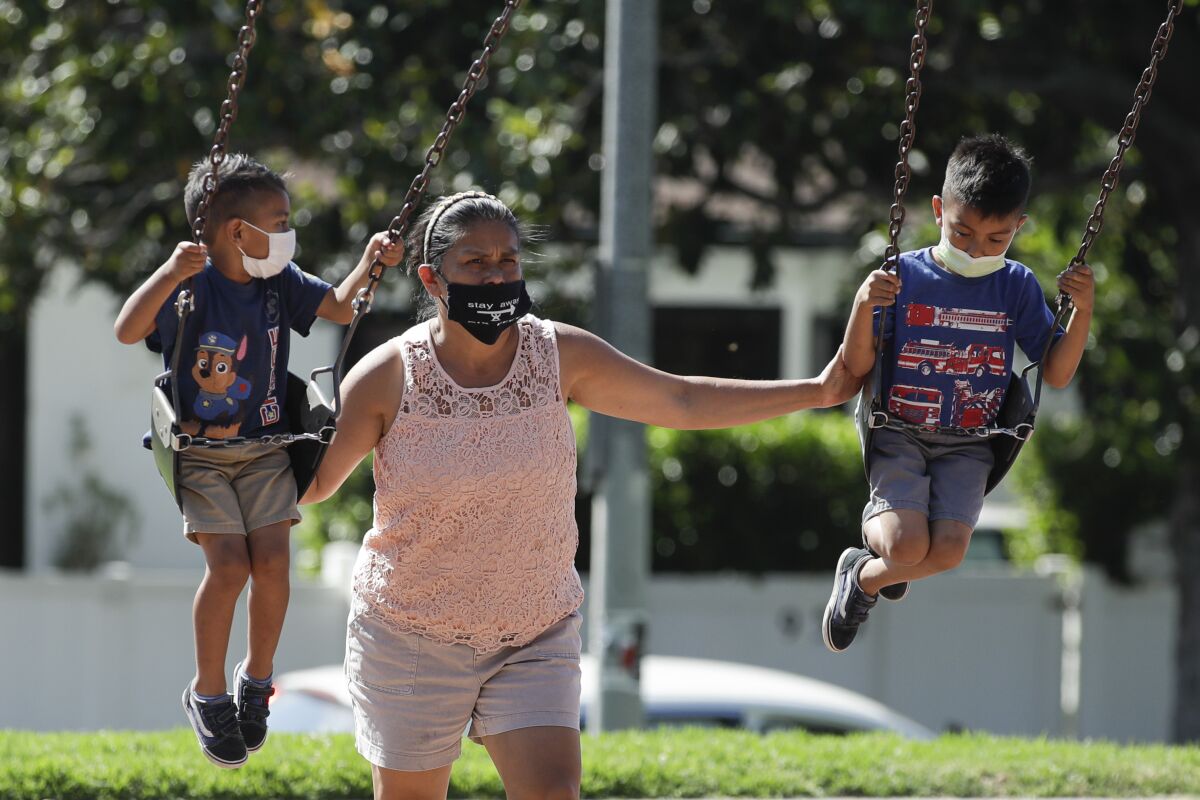 A woman and two children wear masks at a playground in Los Angeles