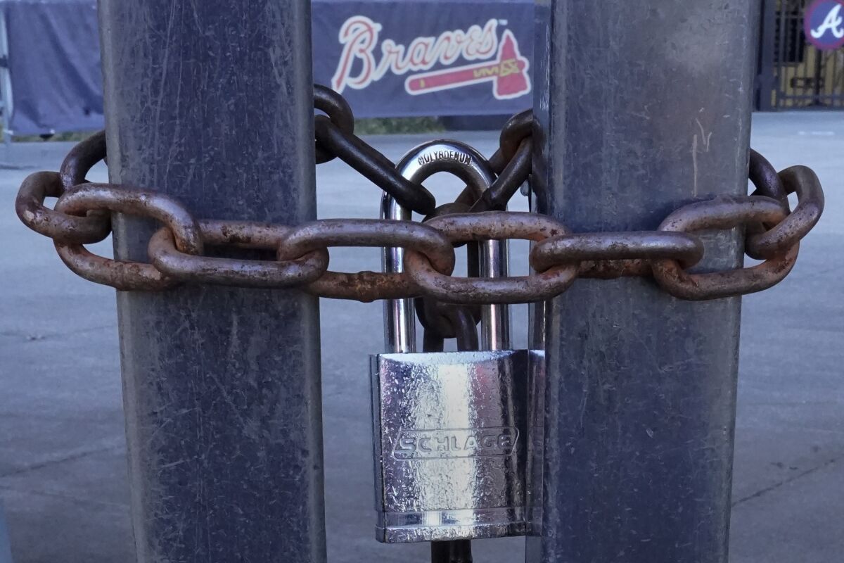 FILE - Locked gates are shown at Truist Park, home of the Atlanta Braves baseball team, Wednesday, March 2, 2022, in Atlanta. Baseball’s ninth work stoppage reached 96 days on Monday, March 7, 2022. It is the sport’s first labor conflict to cause games to be canceled since the 1994-95 strike wiped out the World Series for the first time in 90 years. (AP Photo/John Bazemore, File)