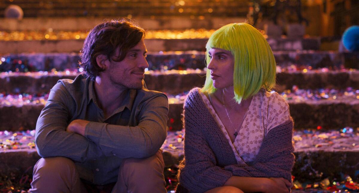 A smiling man and a woman wearing a lime green wig look at each other while sitting on steps.