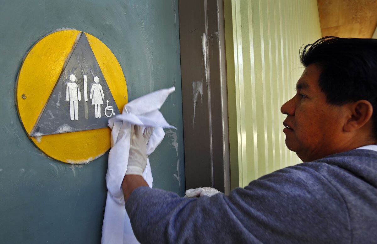 A maintenance worker cleans the front doors of a restroom with a gender-neutral sign in West Hollywood in January. A ballot initiative that sought to require transgender people to use the public restrooms that correspond with their biological sex has failed to qualify for the California ballot, backers say.