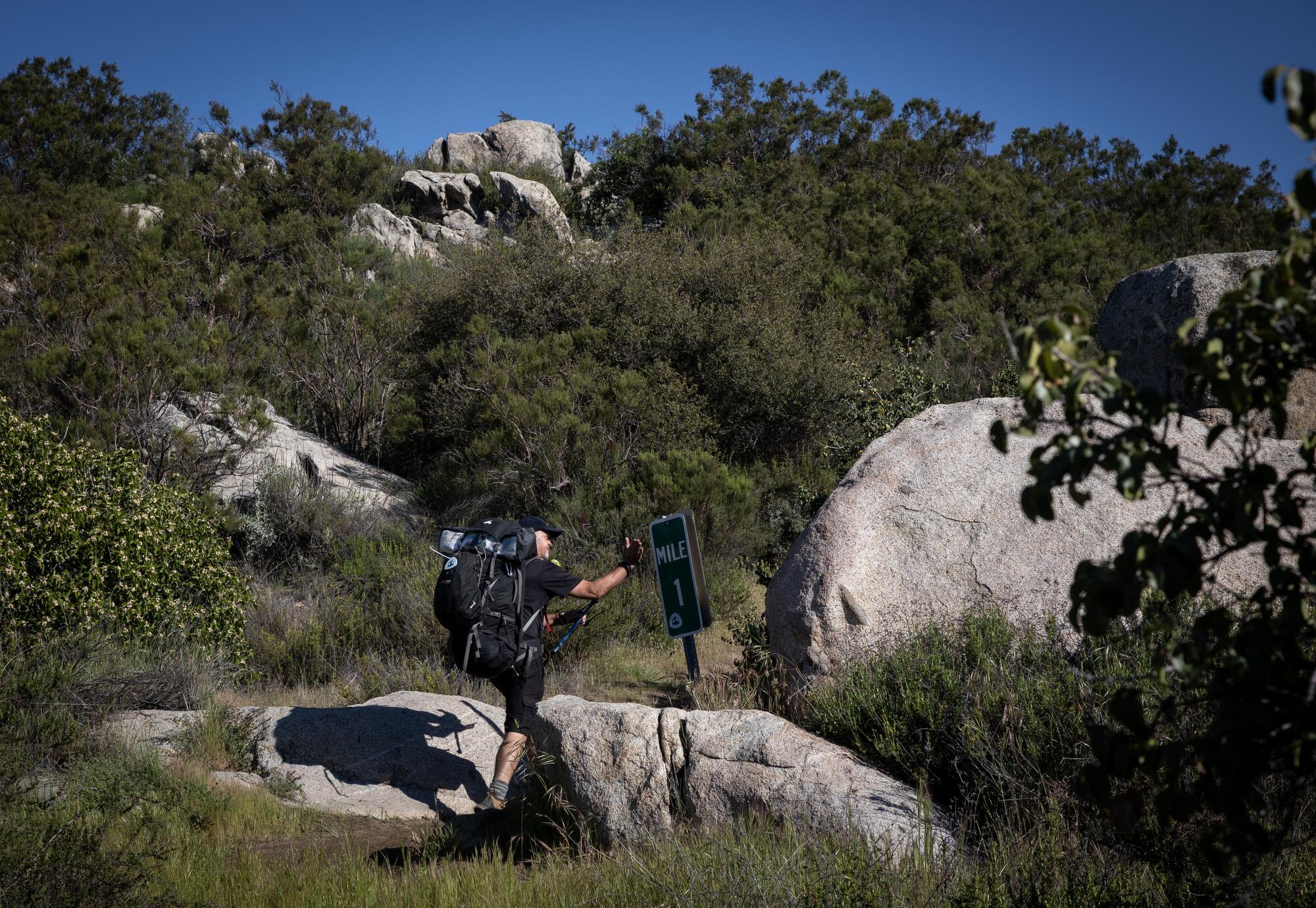 Mike Brown, 52, of New Zealand, touches the mile marker as he hikes the Pacific Crest Trail