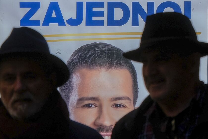 People walk past a pre-election billboard showing Jakov Milatovic, a newcomer supported by the shaky governing coalition with links to neighboring Serbia, in Podgorica, Montenegro, Thursday, March 30, 2023. Voters in small Montenegro go to the polls this weekend to choose their next president in a runoff race between Milo Djukanovic and Jakov Milatovic. (AP Photo/Risto Bozovic)