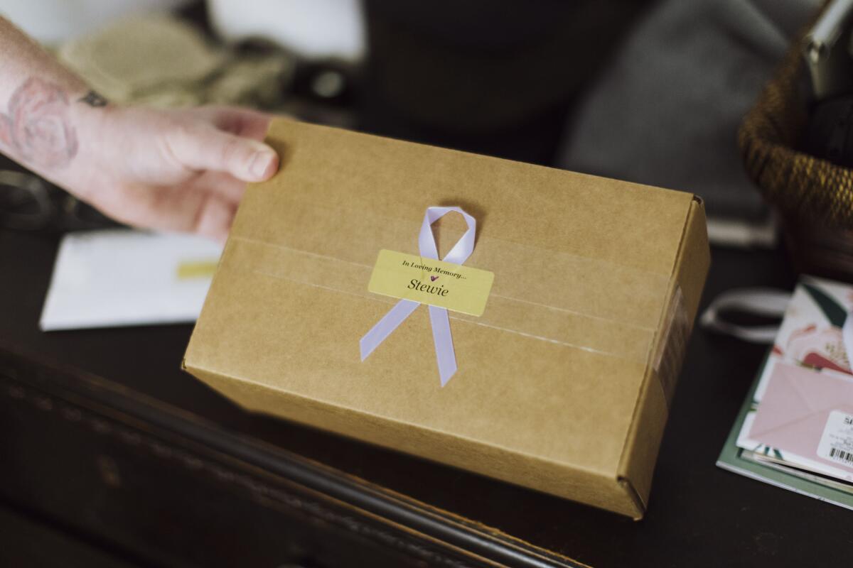 A hand holds a box with a ribbon on it.
