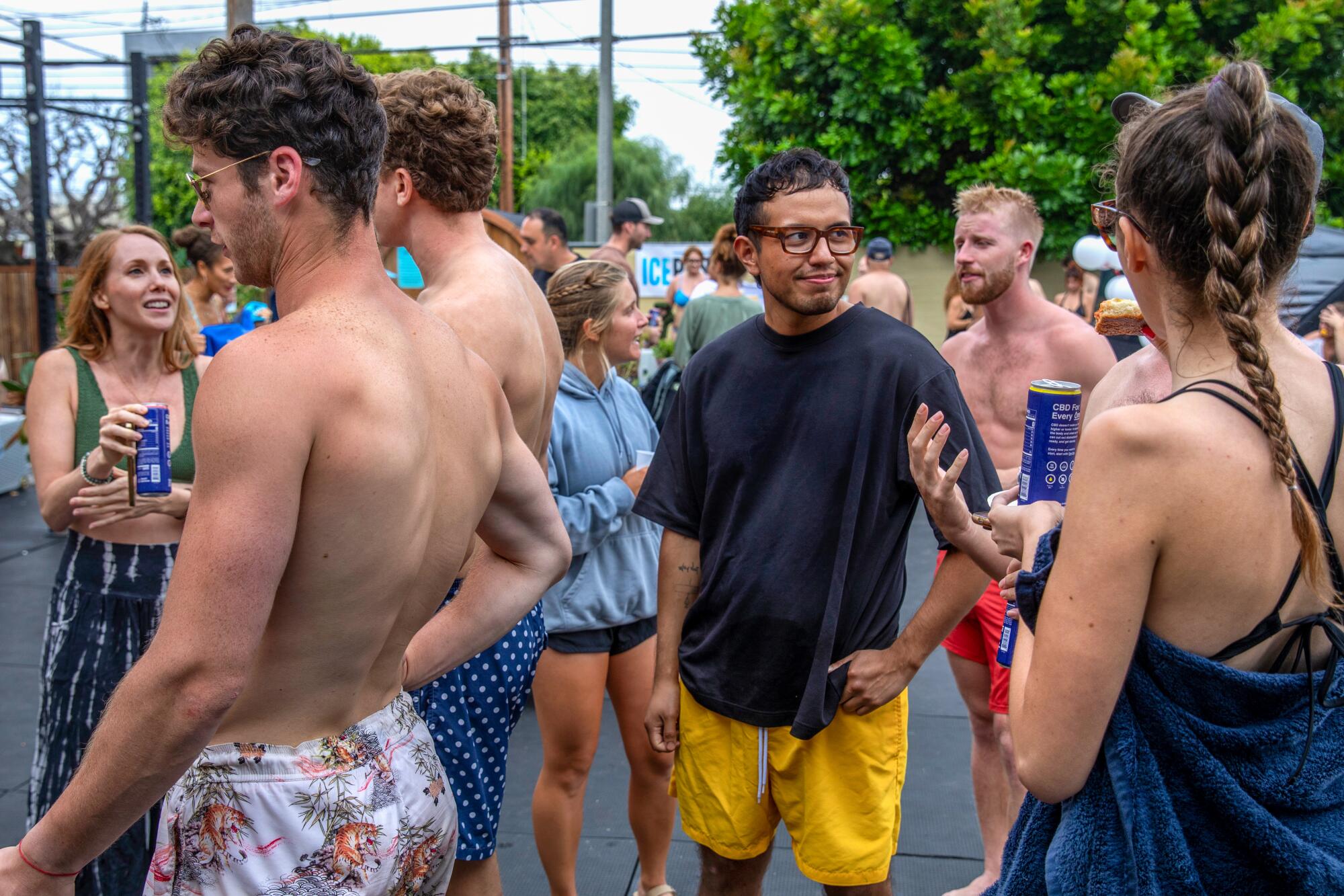 People in bathing suits and trunks stand outdoors talking to one another