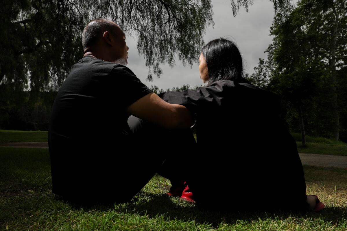 Two people face away while sitting on grass in a park.