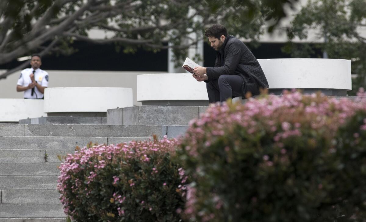 A security guard, left, makes his rounds as a man, right, reads a book at Koreatown's Liberty Park. In recent years, the public hasn't been allowed access to the lawn, with the guard telling visitors the park was "restricted property."