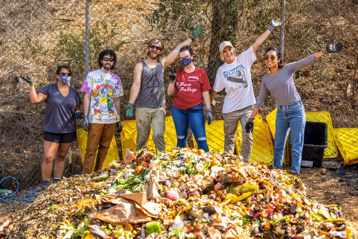 Six people raise their hands to pose in front of a pile of food scraps.