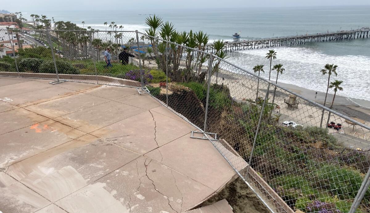 A cracked and broken concrete patio with chain link fence around the edge sits above railroad tracks.