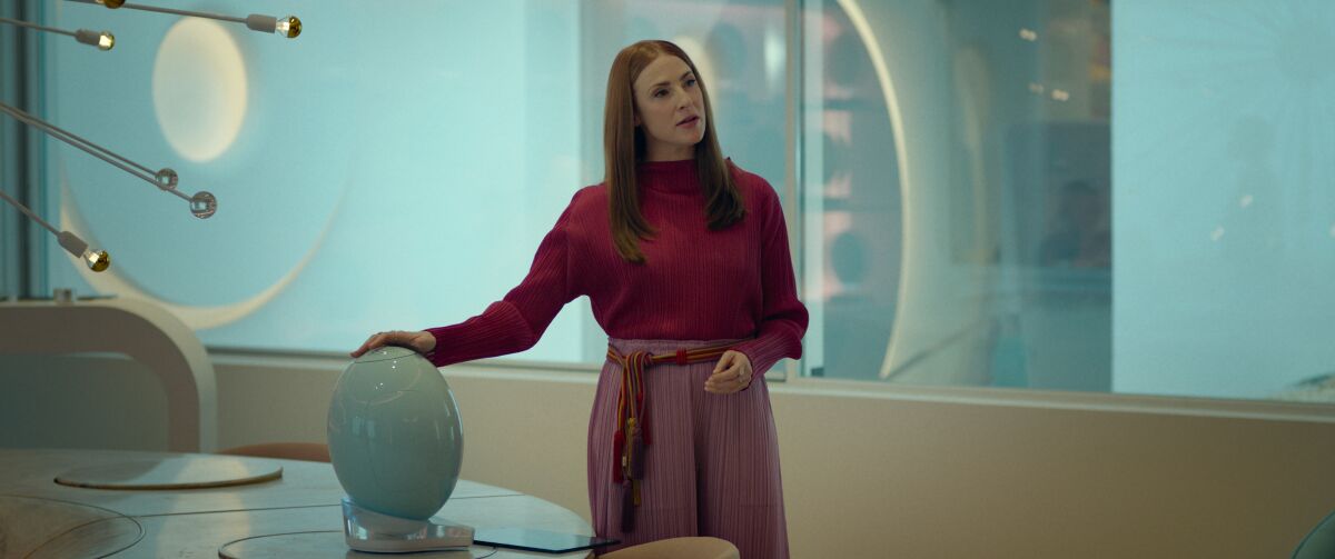 A woman in a red blouse explains a plastic egg-like object.