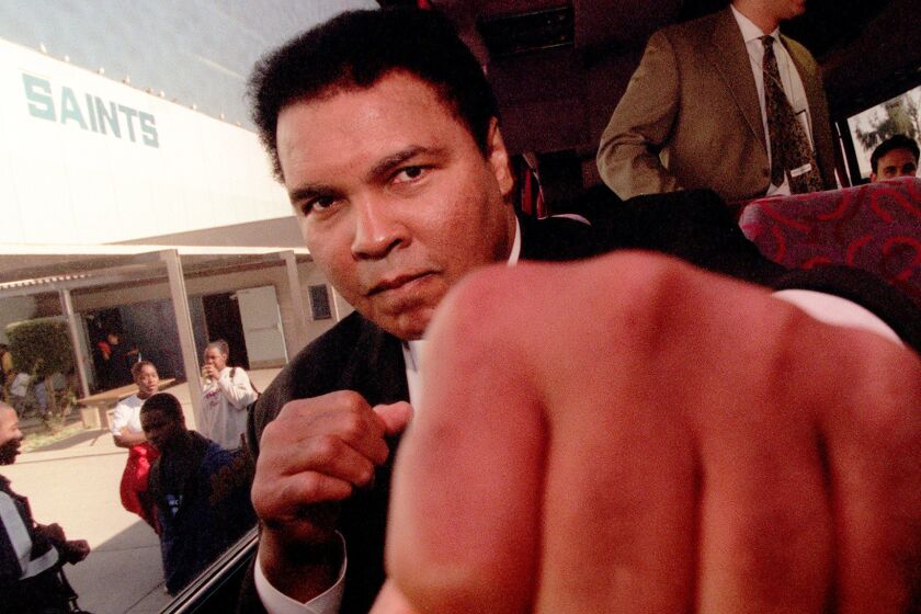 Former heavyweight champion Muhammad Ali throws playful punch toward a photographer while sitting on a bus in front of Locke High School in December 1996.