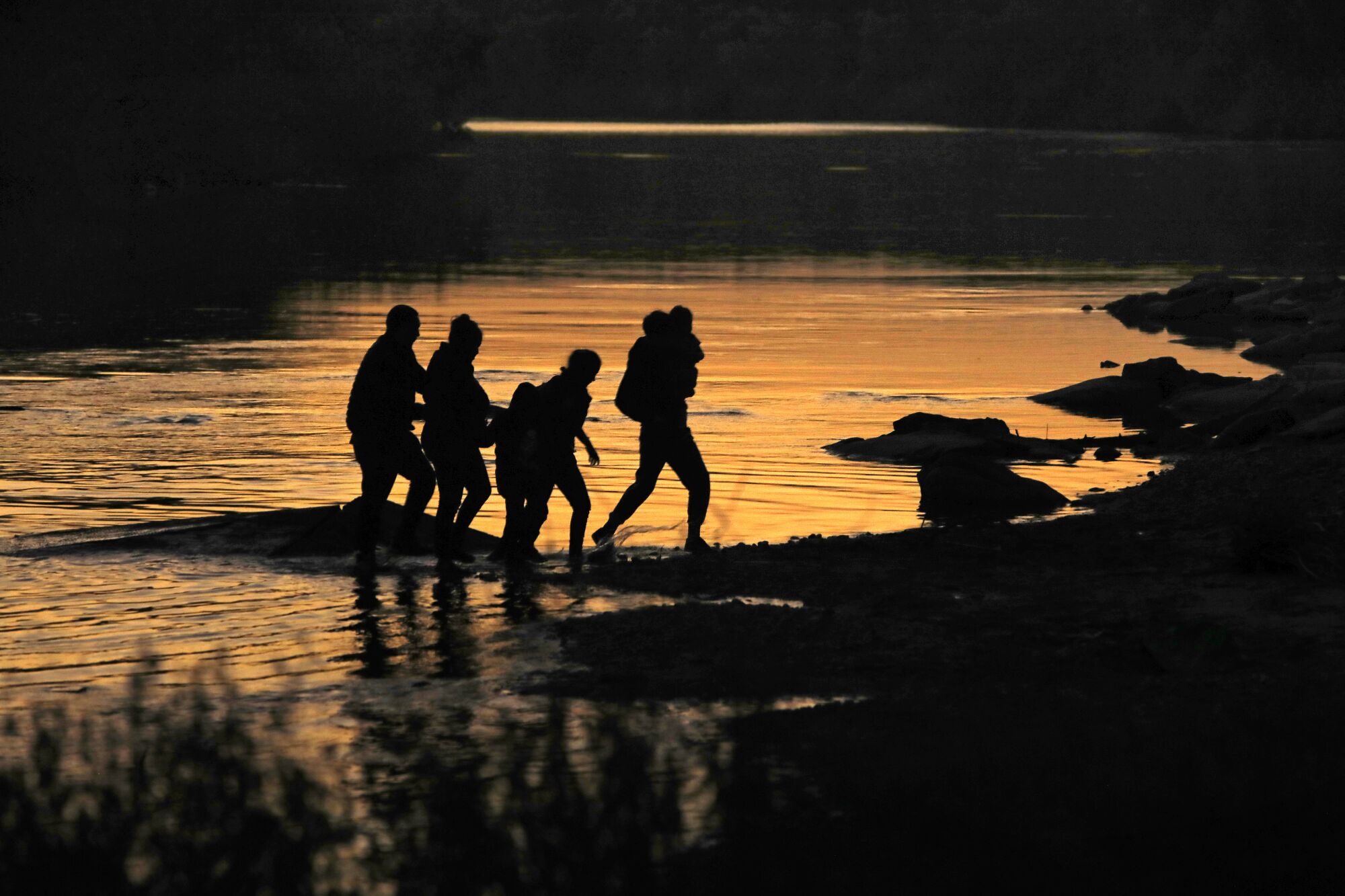 Migrants emerge from the Rio Grande at sunset 