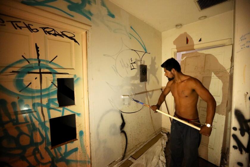LOS ANGELES, CA - DECEMBER 1, 2021 - Alex Seijas Torres, 24, paints over graffiti inside the room where he resides in an abandoned building that once housed the Vermont Dental Implant Center in Koreatown on December 1, 2021. He has been making repairs to his space. Torres has been living at the site, with his dog Wolf, for the past two months. Torres has wired electricity into the building from an outside pole so he can power a small refrigerator, microwave, stereo and a few lights. He gets water from the fire sprinklers so he can wash up and also bath his dog. A community of homeless people are living in the building that has been abandoned for 3 to 4 years, locals said. They all have their own rooms in the building that has been red tagged by the city. (Genaro Molina / Los Angeles Times)