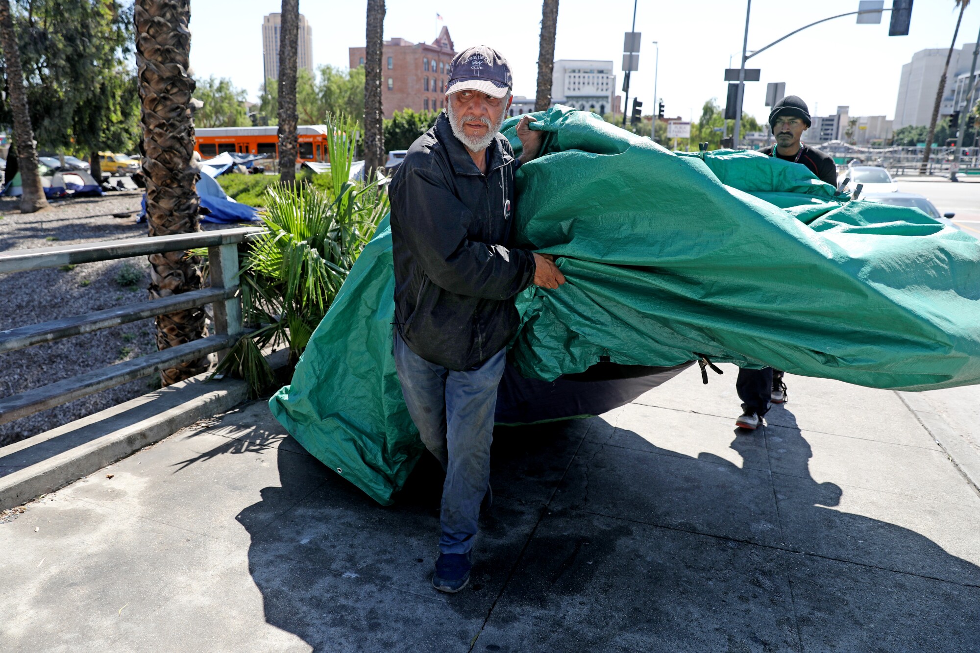 A man gets help carrying a large green tarp down a sidewalk.