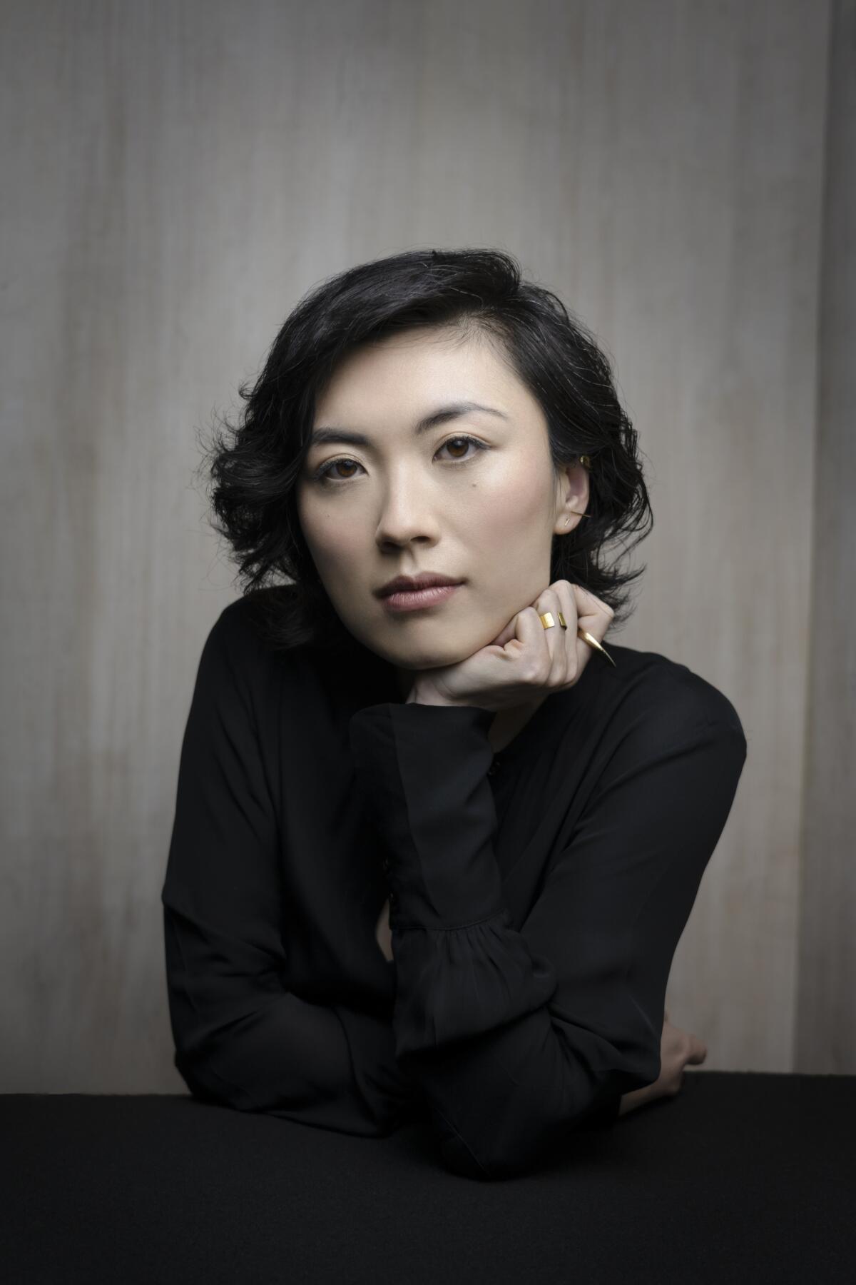 A woman with chin length hair poses in a thin black sweater.