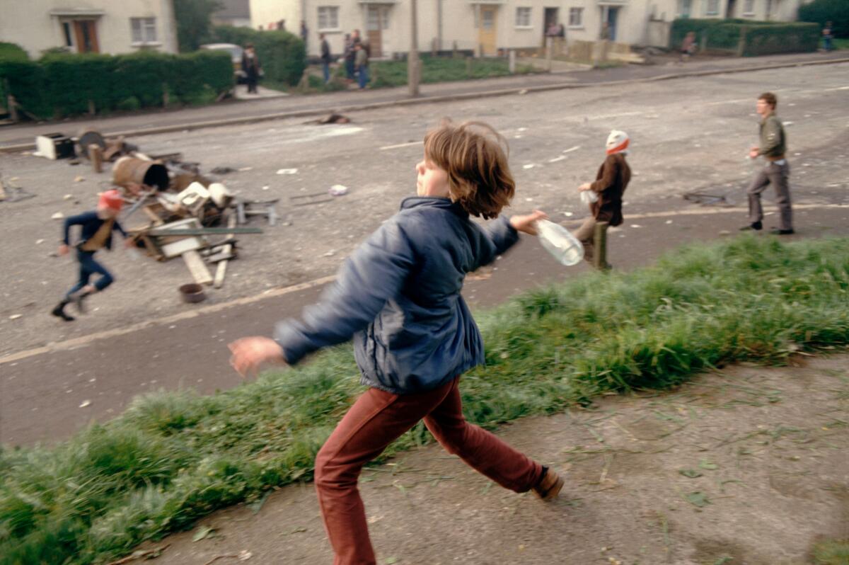 A young rioter throws a bottle from a hillside during the 1981 Belfast riots.