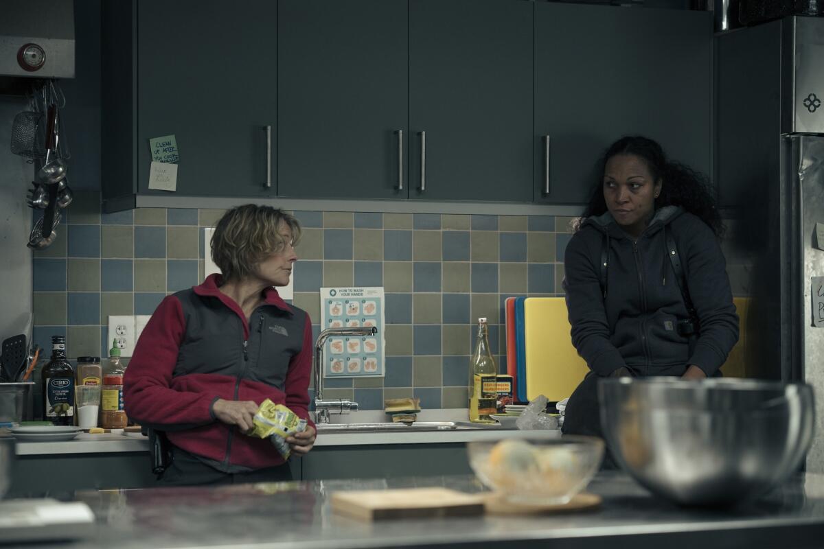 Two women standing in a kitchen look at one another.