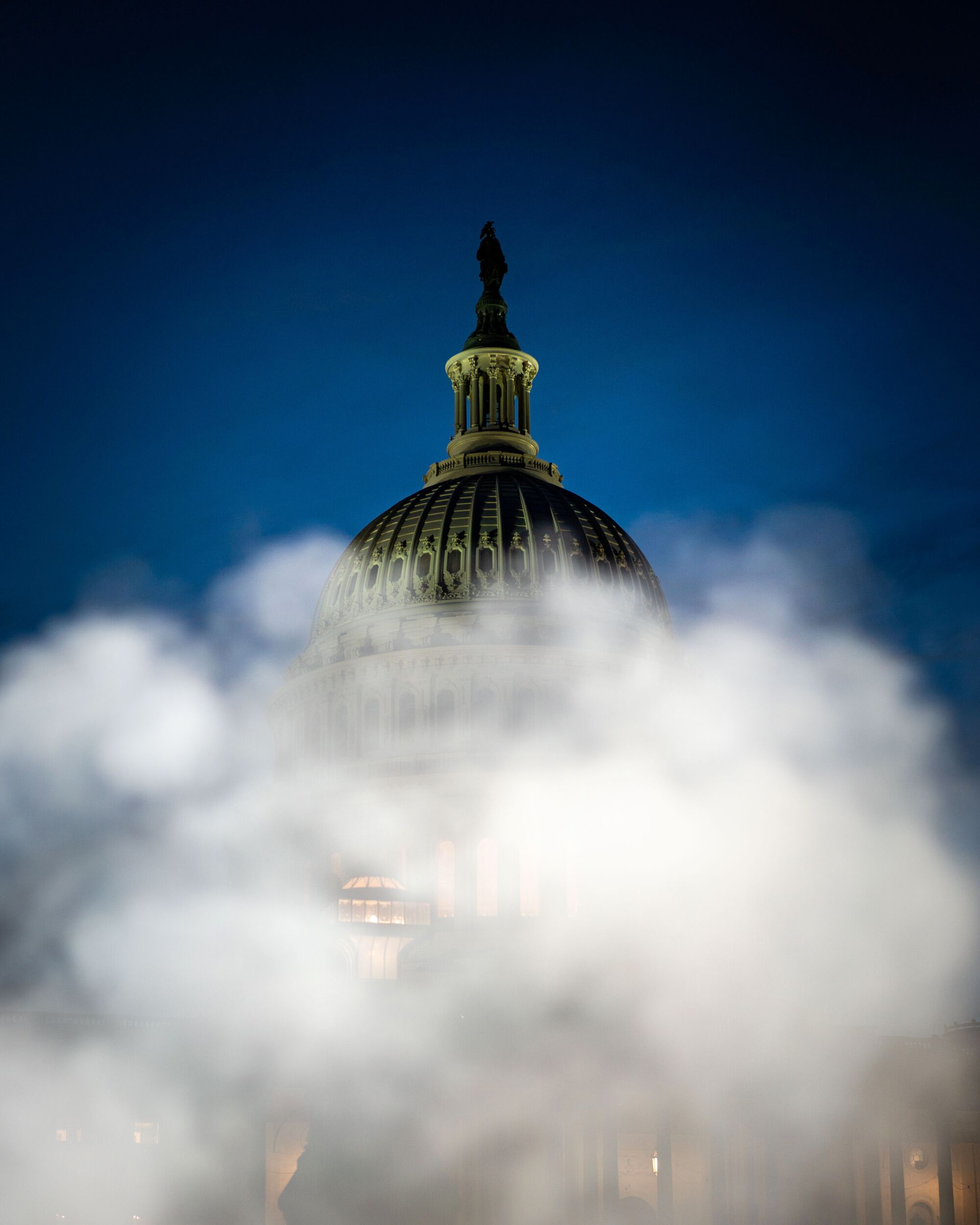 A vertical, twilight frame of the U.S. Capitol rotunda tower partially obscured by steam.