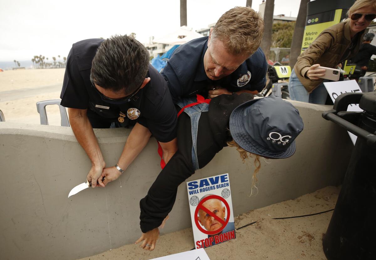 A woman is pinned against a concrete bench by two officers, who clutch a knife they've pulled from her hand.