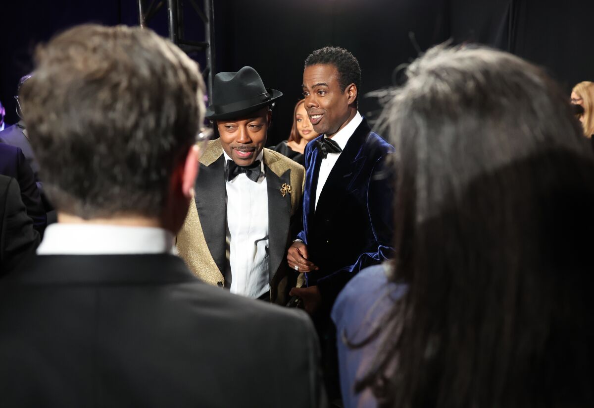 Two men in tuxedos stand in a crowd backstage.