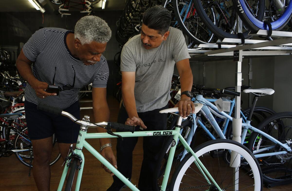 Rikki Williams, a fixed gear bike fan, examines a fixie with employee Juan Reyes at the Just Ride L.A. bike shop. Williams has been riding a fixed gear bike since 2012.