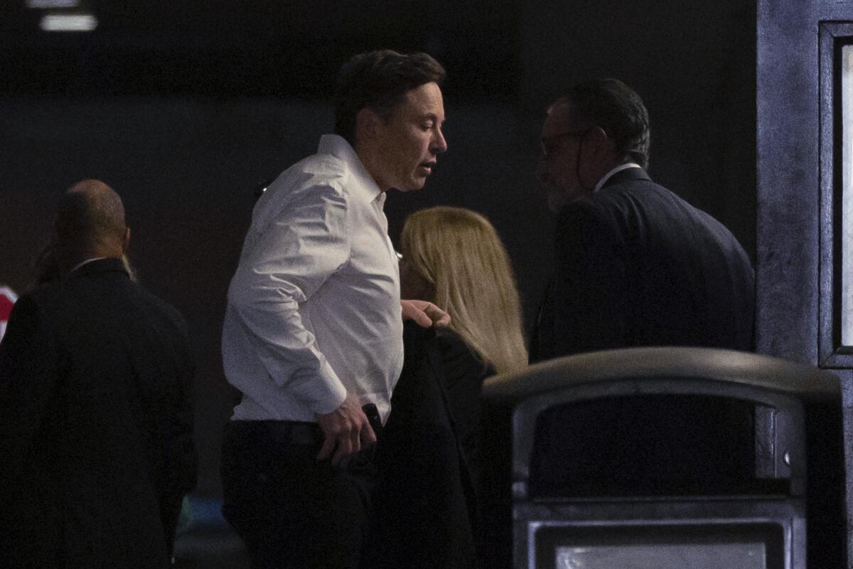 Elon Musk is shown wearing a white shirt and carrying a jacket.