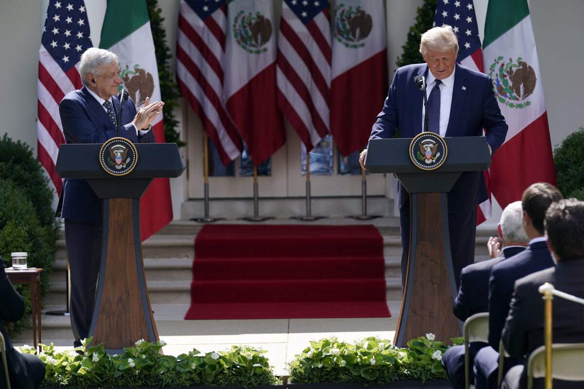 A man in a dark suit and tie, standing at a lectern, left, applauds as another man in a suit and tie speaks at a lectern
