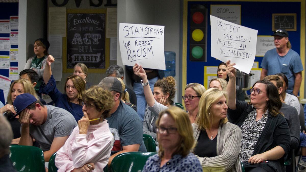 Trina Trac, left, and Rachel Potucek hold signs up during the public comments section of an Ocean View School Board meeting on Tuesday.