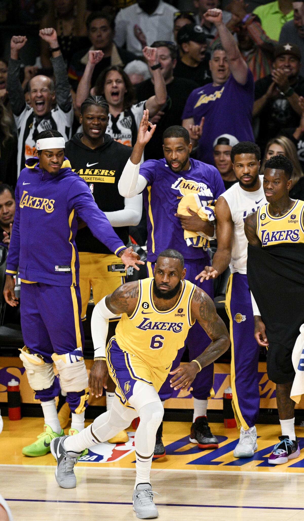 Fans react in the background as Lakers forward LeBron James sprints up court after making a three-point shot.