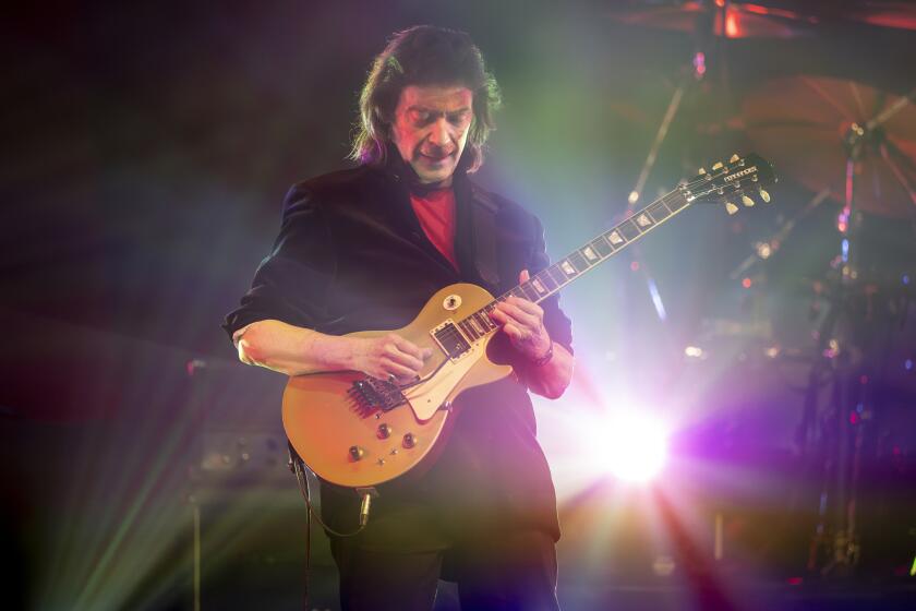  Steve Hackett plays guitar onstage with a light shining behind him