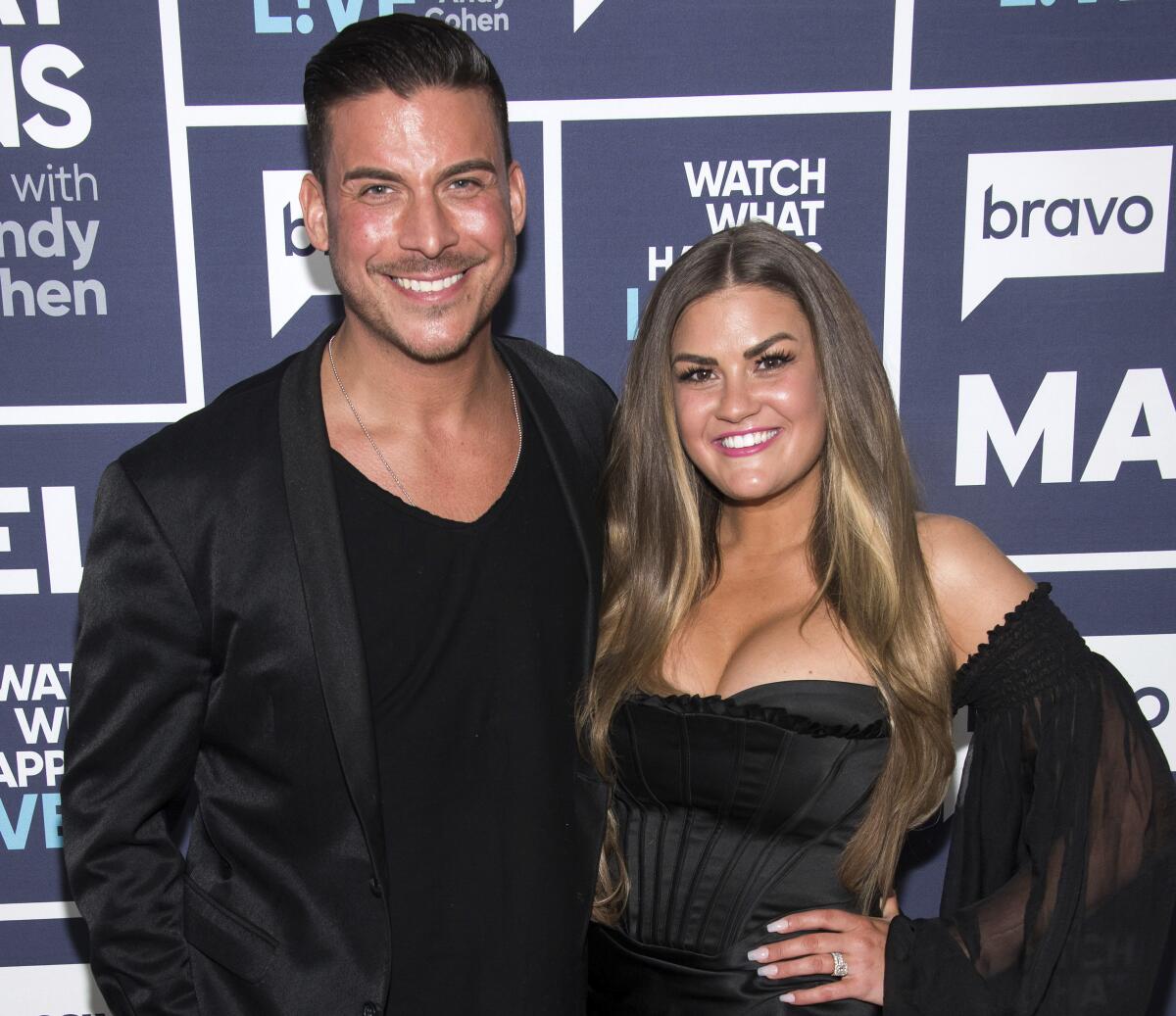 Jax Taylor standing in a black jacket over a black T-shirt with his arm around Brittany Cartwright in a strapless black dress