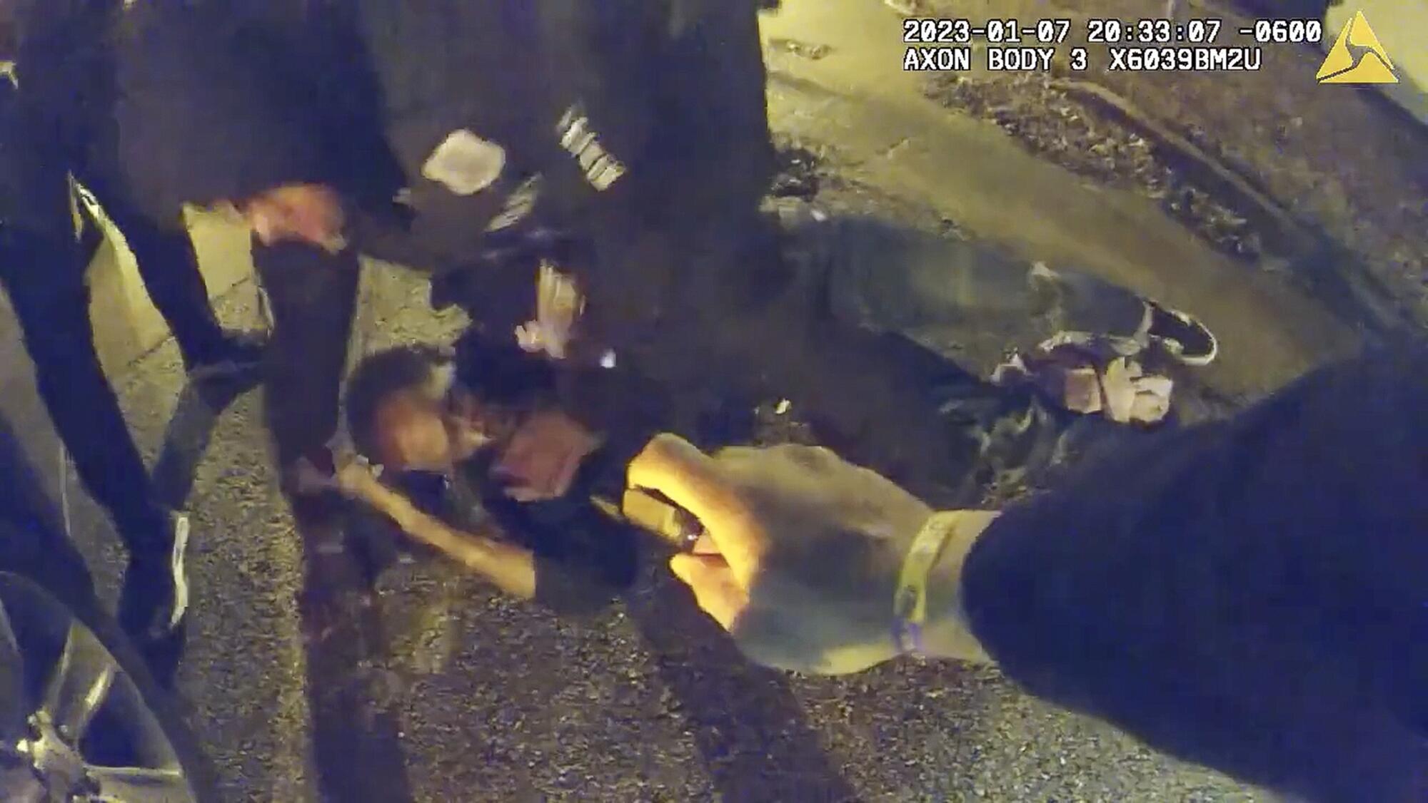 A man cowers on the ground while being pepper-sprayed and restrained by police.