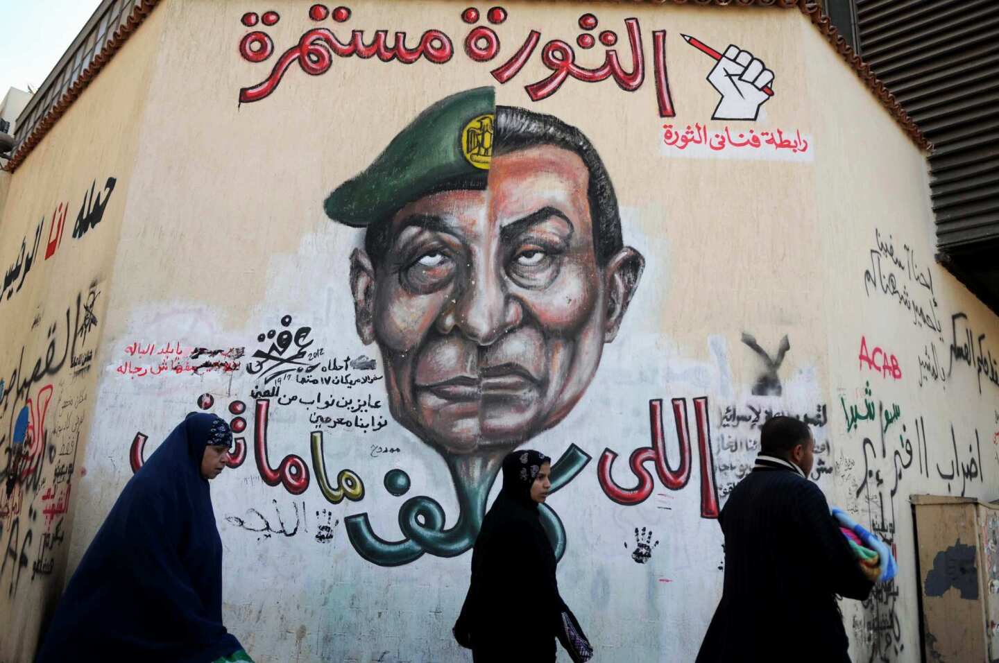Egyptians in Cairo's Tahrir Square walk past graffiti of a head composed of the faces of ousted President Hosni Mubarak, right, and Field Marshal Mohamed Hussein Tantawi, leader of Egypt's ruling military council, with a slogan reading, "The revolution continues."