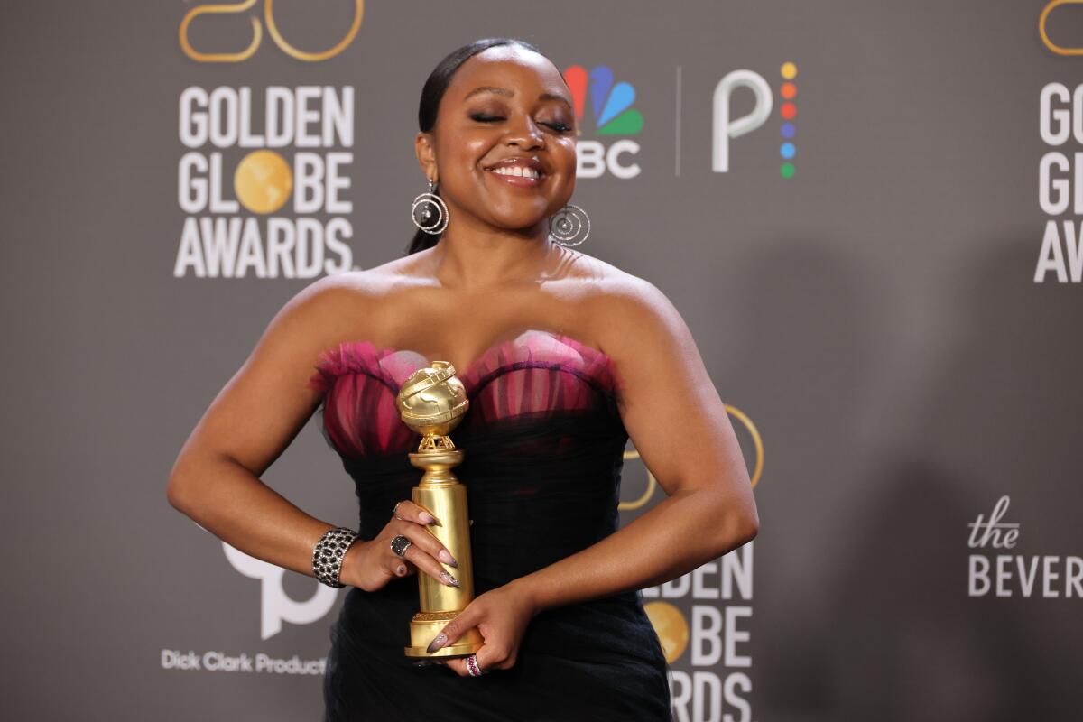 A smiling woman holds a Golden Globe statue