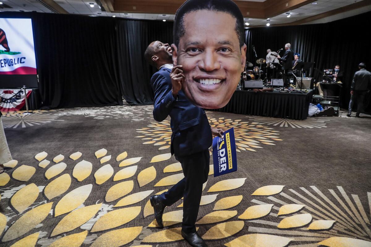 Errol Webber of Costa Mesa carries a cutout picture of Larry Elder at the candidates' election party 