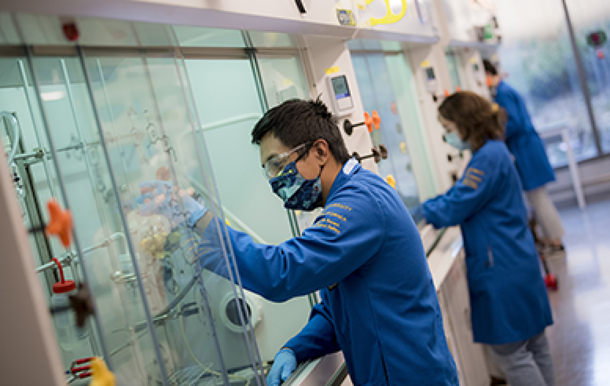 Students in blue lab coats work with equipment.