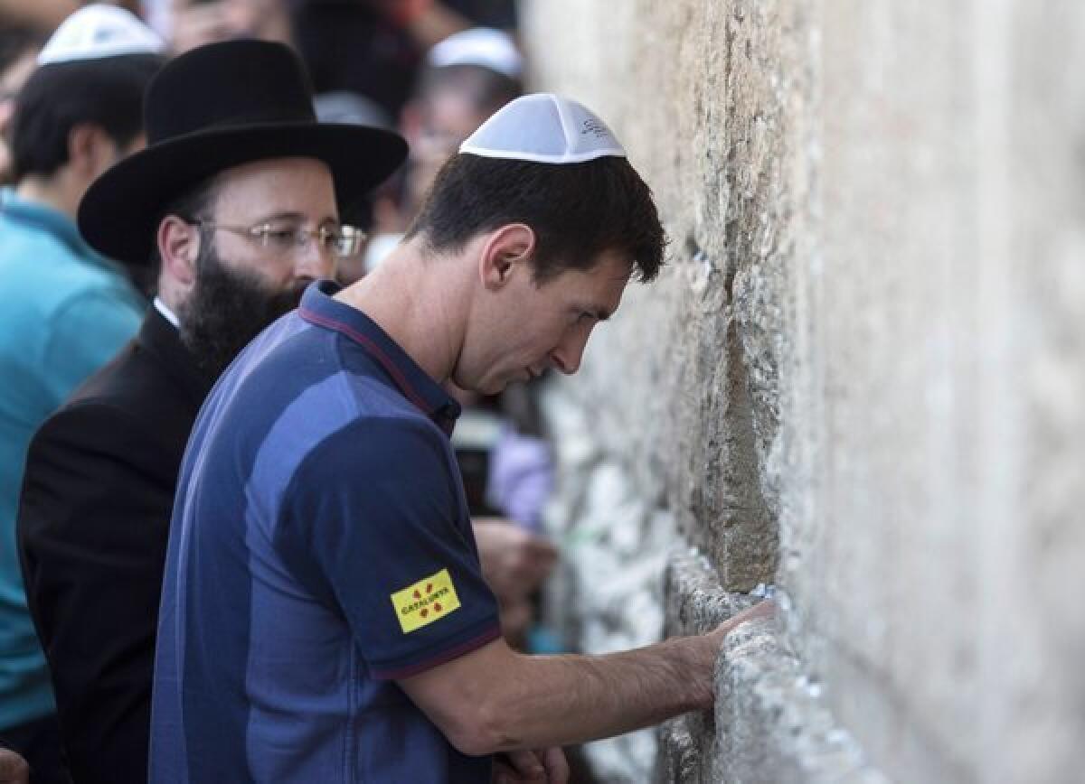 FC Barcelona soccer star Lionel Messi puts a paper with wishes in a crack in the Western Wall in Jerusalem on Sunday. A Facebook post joked that Prime Minister Benjamin Netanyahu offered Messi a job as head of the Bank of Israel, which he is having considerable difficulty filling.