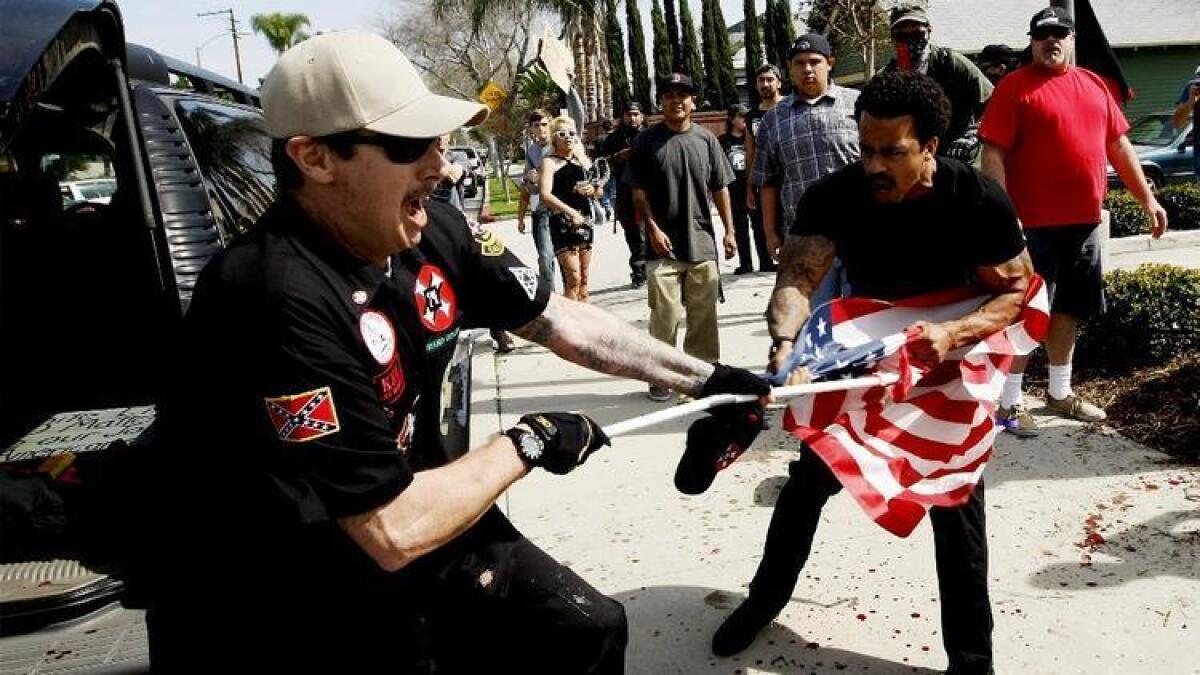 Un hombre del Ku Klux Klan (izq.) pelea contra un manifestante por una bandera de los EE.UU., luego de que miembros del KKK intentaran realizar una marcha en Pearson Park, Anaheim, en febrero pasado. Siete de los manifestantes fueron ahora acusados de atacar a los miembros del Klan.