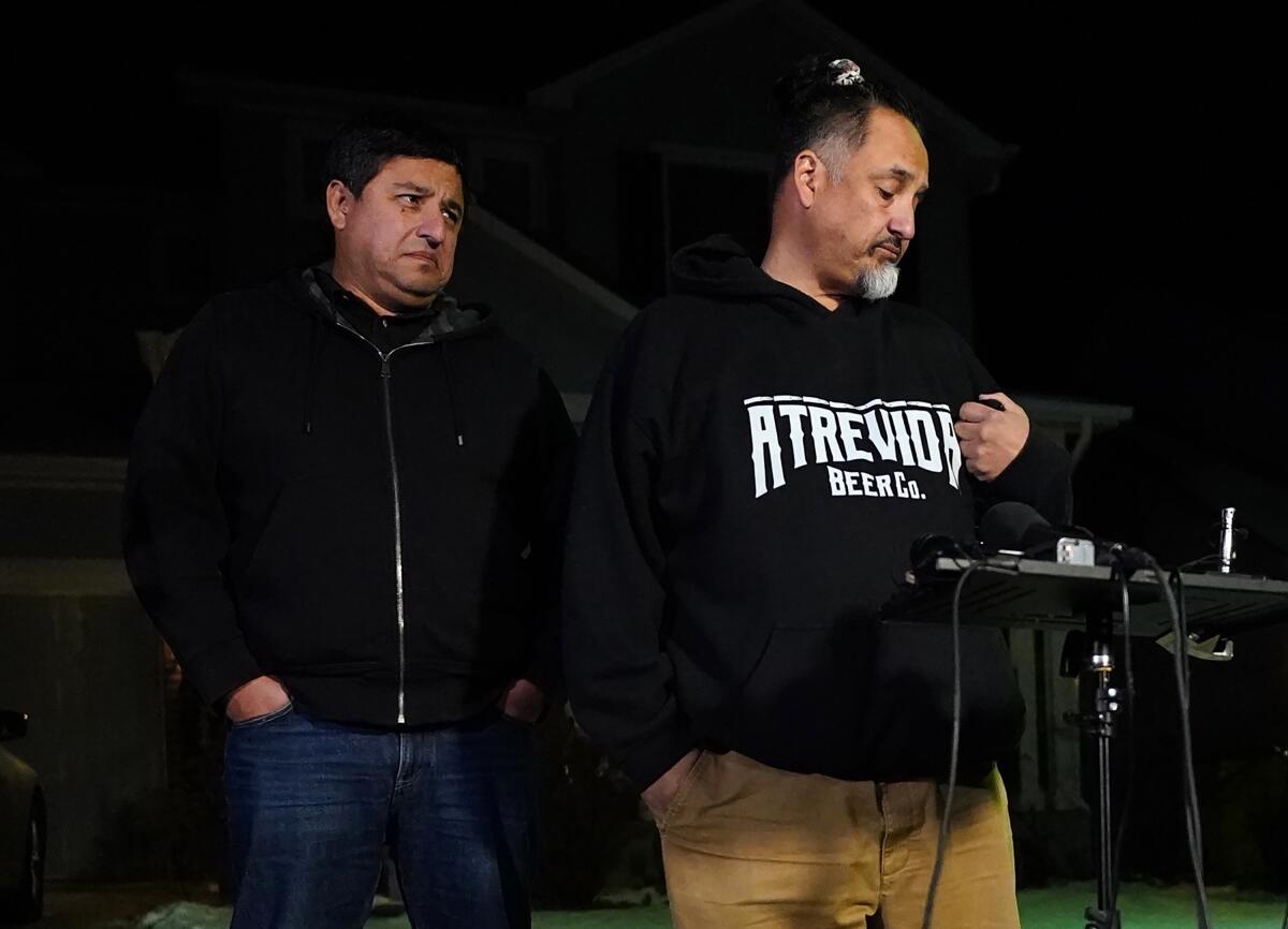 Two men with somber expressions stand near a microphone 