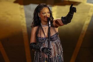 A woman in a sparkling gown raises her hand onstage