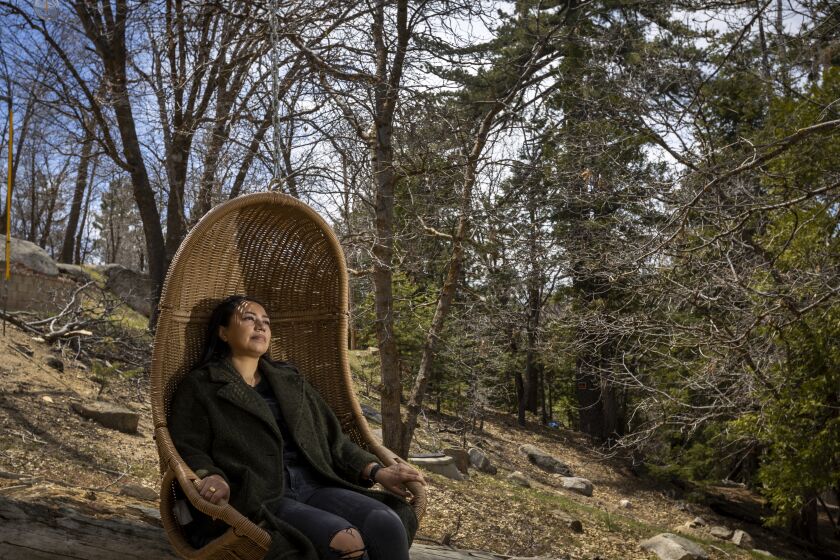 Lake Arrowhead, CA - April 26: Natalie Camunas relaxes in a swing chair outside her and her partner's cabin in Lake Arrowhead Tuesday, April 26, 2022. When the 35-year-old and her partner purchased a small cabin in the mountains two years ago, they had intended to use it as an investment property that they would rent out to vacationers looking for a forest escape. The couple bought the 670-square-foot home for $189,000, Camunas said, when housing prices in Southern California were climbing, but before they smashed records and hit an all-time high. But after quarantining in their apartment in Los Angeles's Fairfax district as the COVID-19 pandemic spread, discovering dead rats in their home and dealing with a bug infestation, they decided to make their move to San Bernardino County official in the fall of 2020. (Allen J. Schaben / Los Angeles Times)