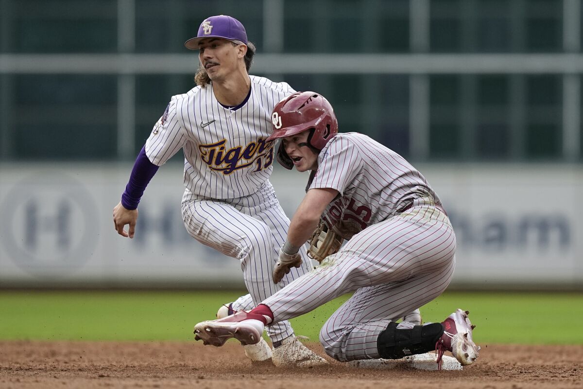Oklahoma's Jackson Nicklaus (15) is tagged out at second by LSU's Jordan Thompson (13) while trying to stretch a single into a double during an NCAA college baseball game at Minute Maid Park, home of the Houston Astros, Friday, March 4, 2022, in Houston. College baseball might turn out to be an attractive alternative for baseball fans if the Major League Baseball lockout extends deep into the spring. (AP Photo/David J. Phillip)