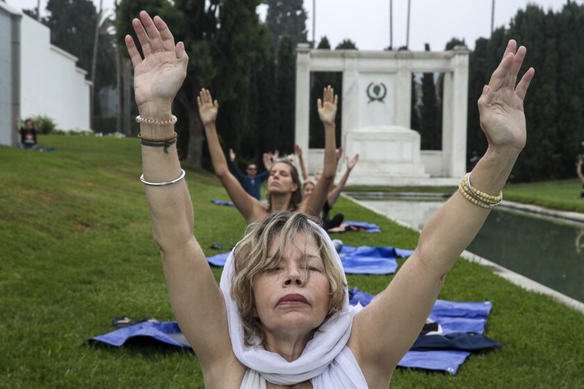 People close their eyes and rise their hands as they sit outside on yoga mats 