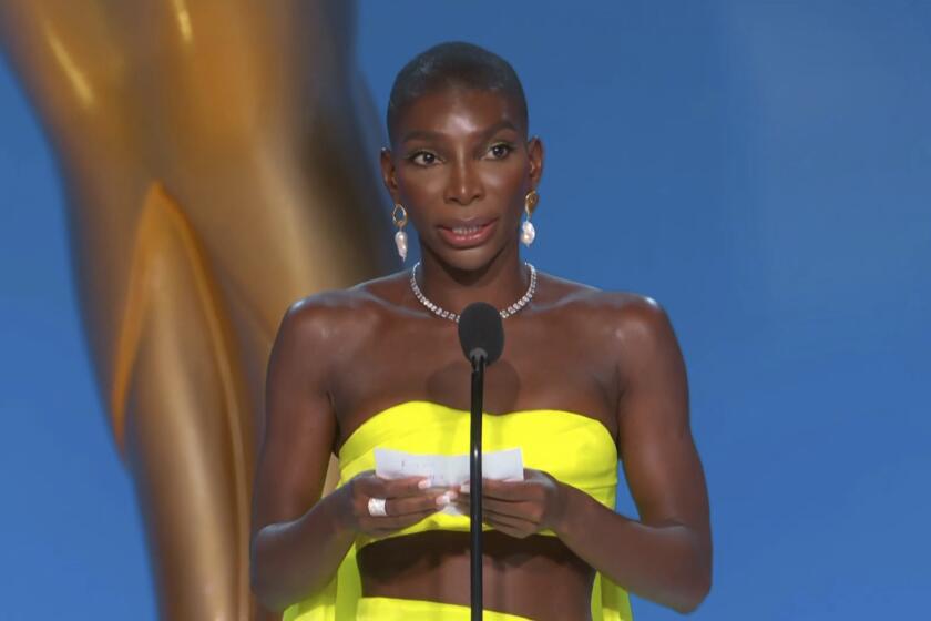 A woman in a bright yellow dress holding a piece of paper and speaking into a microphone