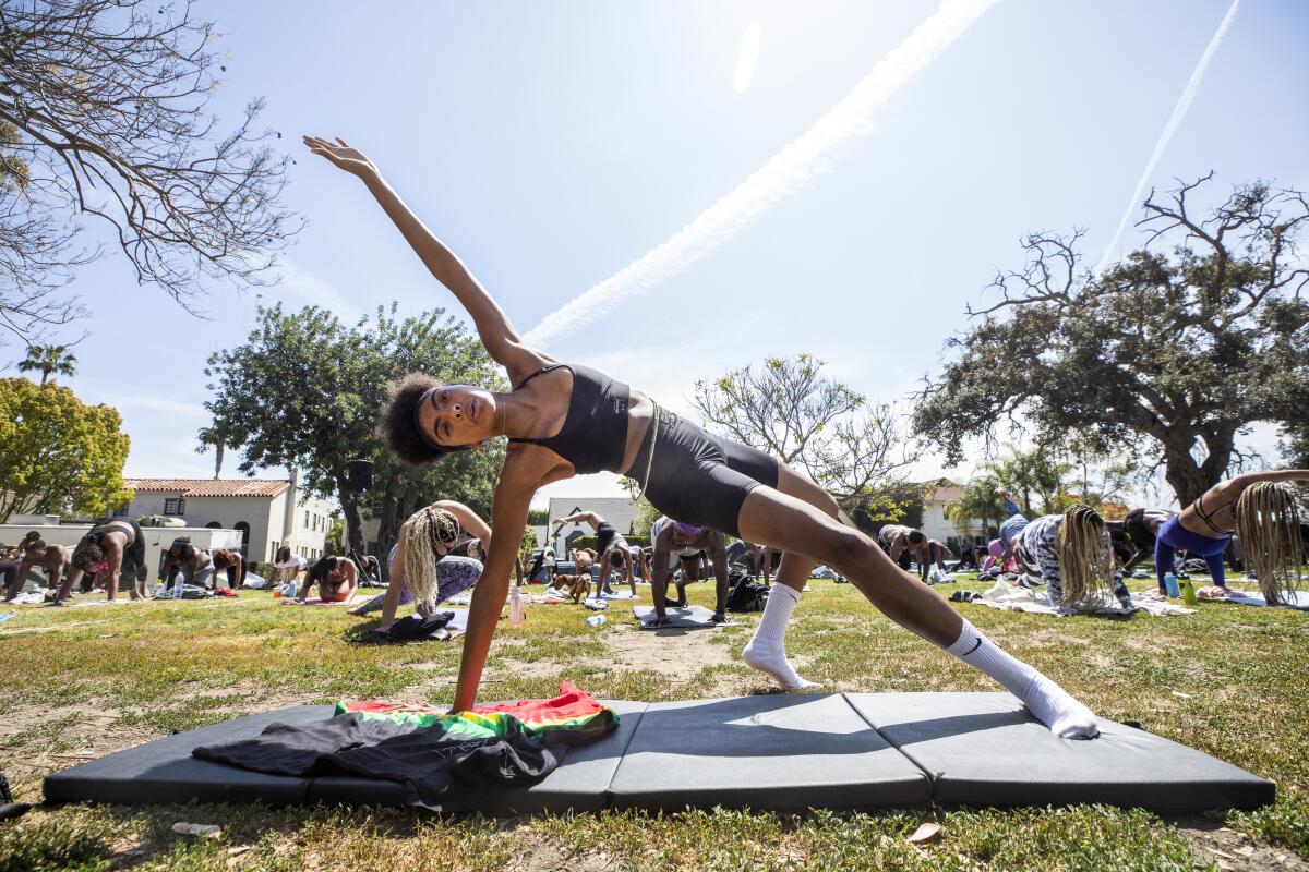 A woman in front of a large crowd of people, all doing yoga in a park.