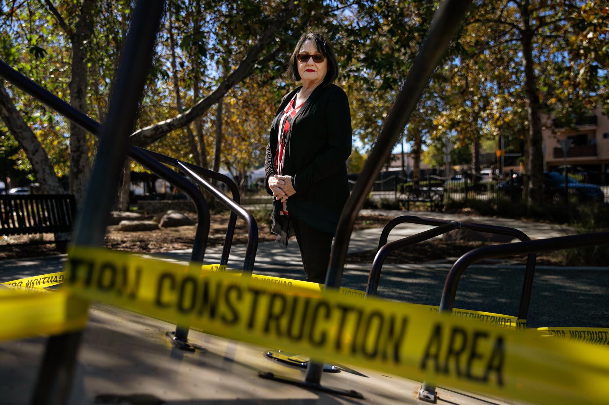 A woman stands next to playground equipment blocked off by yellow "construction area" tape.