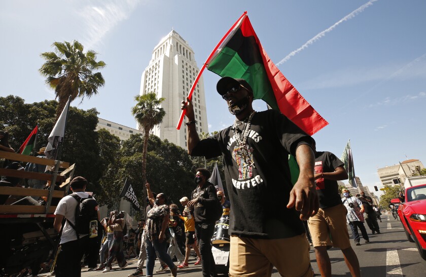 A man in a Black Lives Matter T-shirt and holding a Pan-African flag walks with other people down a city street.