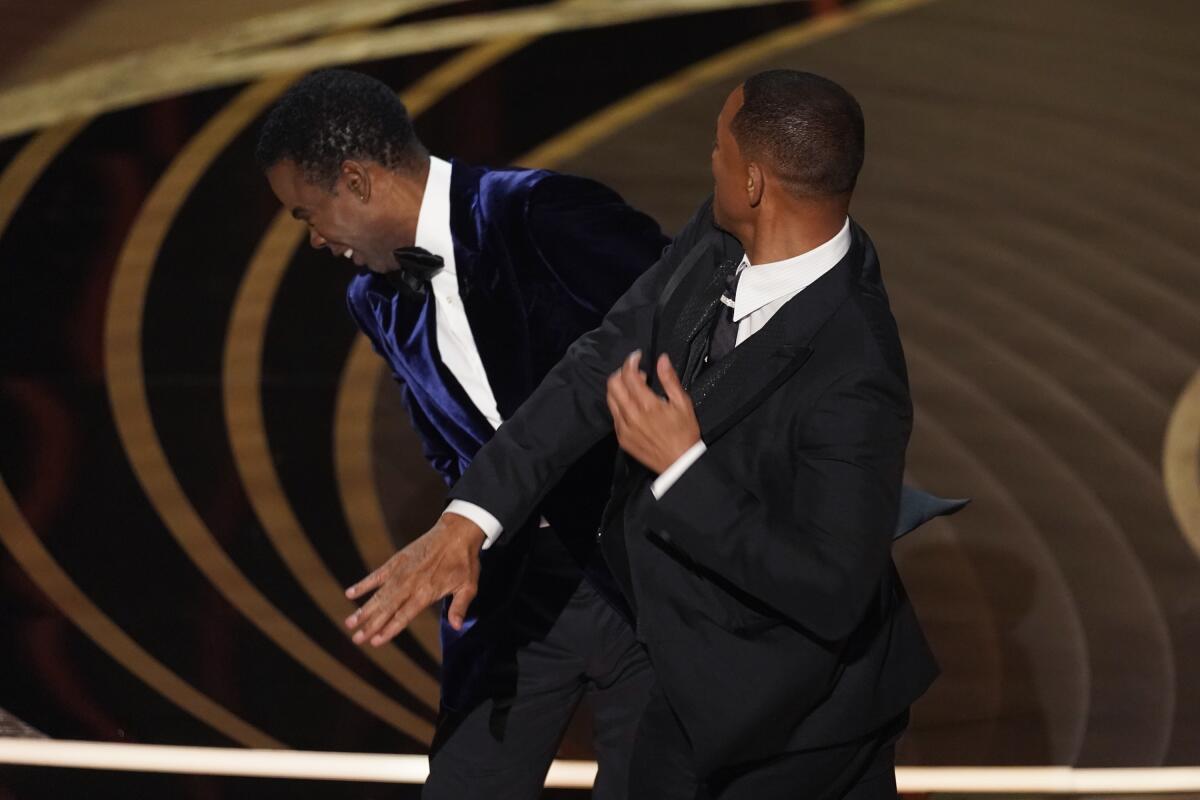 Will Smith, right, hits presenter Chris Rock on stage while presenting the award for best documentary feature.