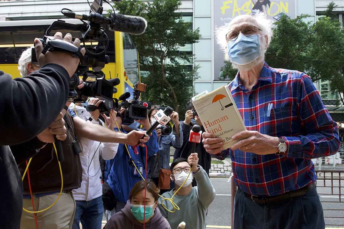 John Clancey, holding a book, stands in front of media holding cameras and microphones.